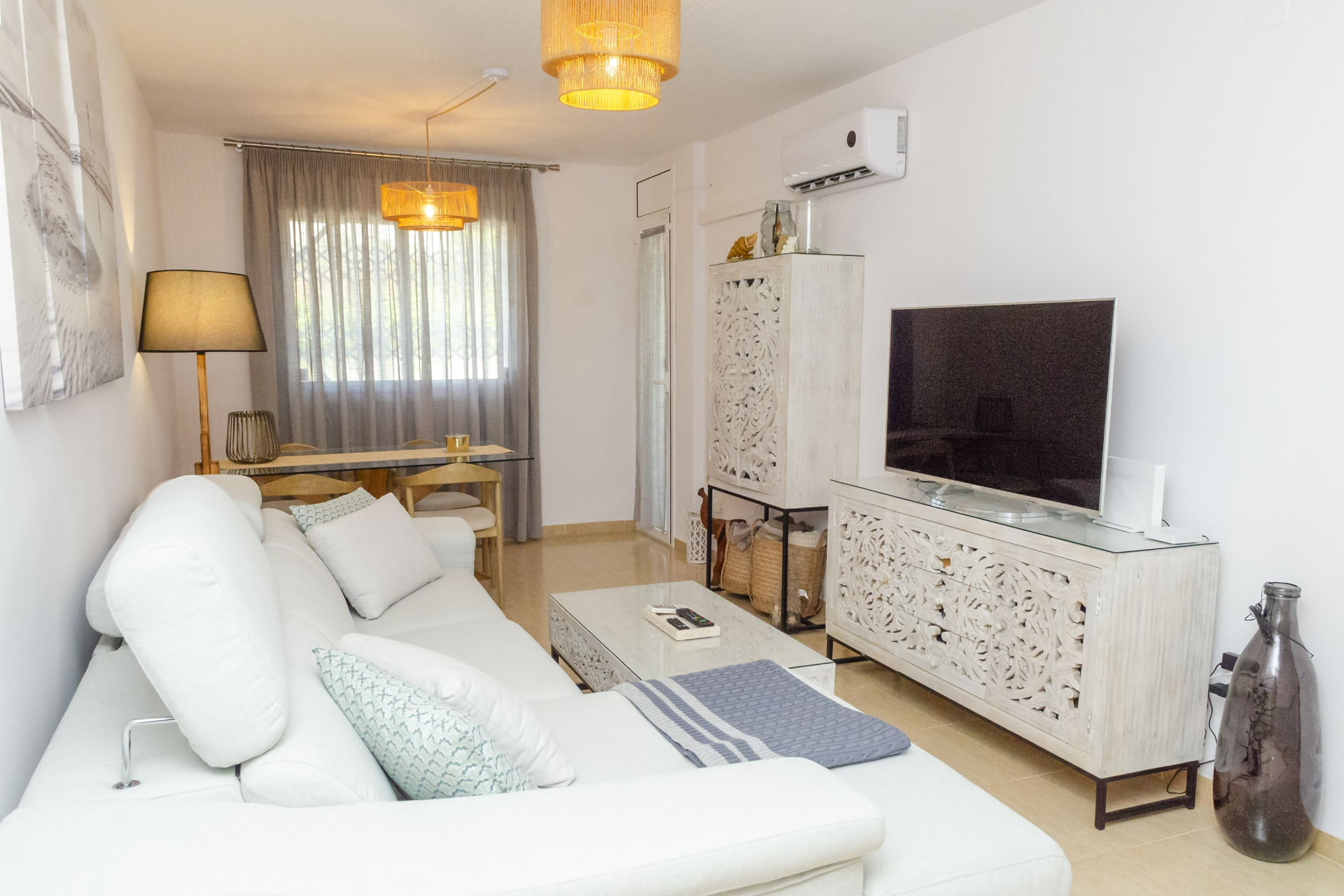 Salón comedor luminoso con sofá blanco, televisión y mesa de comedor